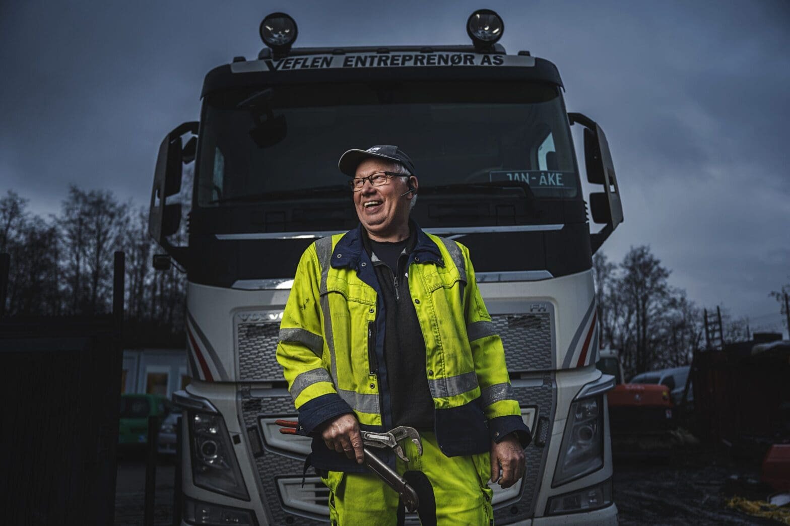 Bilde av en mann med rørlegger verktøy i hånda, foran en lastebil