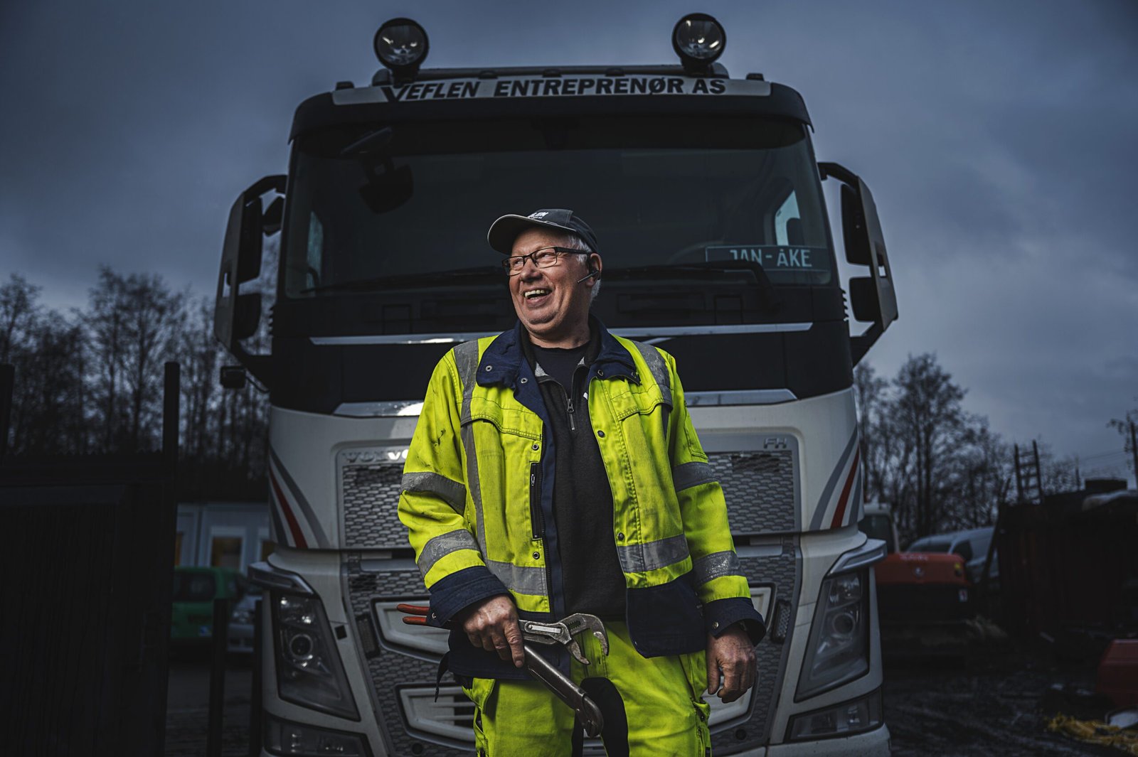 Bilde av en mann med rørlegger verktøy i hånda, foran en lastebil