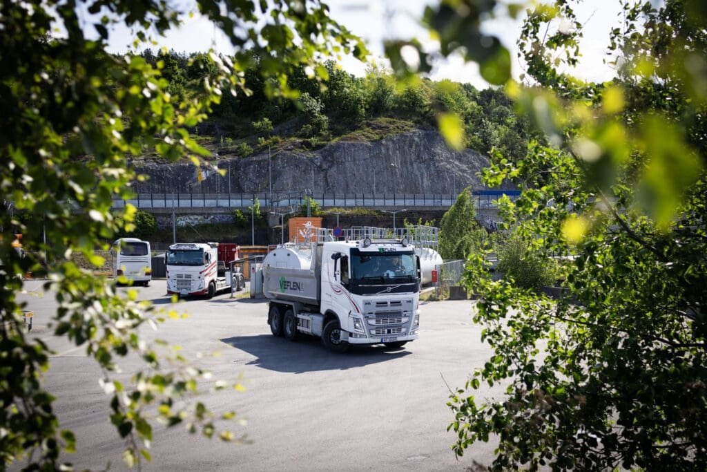 Veflen lastebil kjører inn på anleggsområde omgitt av grøntområder.
